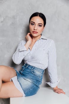 fashionable woman in a denim skirt sits on a chair with a gray background