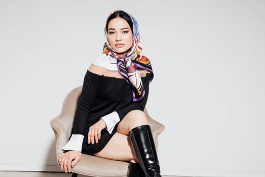 beautiful woman in a colored scarf and in a black dress sits on a chair leg to foot