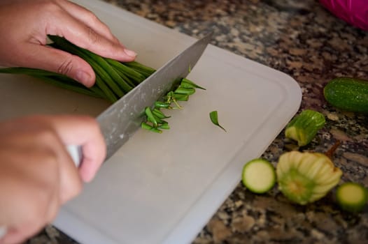 Close-up view of a housewife, woman chef cook holding a kitchen knife, slicing fresh green beans on a cutting board, standing by marble kitchen counter in the home kitchen. Raw food. Vegetarianism.