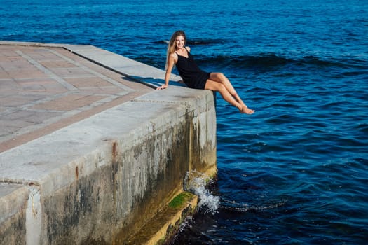 a woman sitting on a concrete slab near the sea walking beach rest