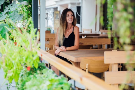 woman sits in a restaurant on a veranda outside waiting for food