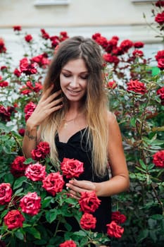 woman stands in the rose bushes in the park on the street walk