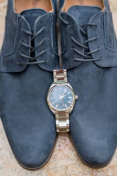 Man watch lies on blue men lace-up shoes standing on a marble floor. High quality photo