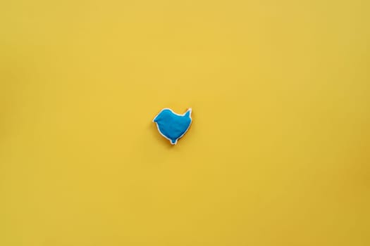 Glazed blue gingerbread bird lies in the center on a yellow background. High quality photo