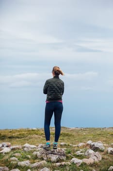 woman on the mountain stands with her back and looks up at the sky