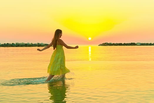 beautiful girl in a yellow dress running on the water at dawn