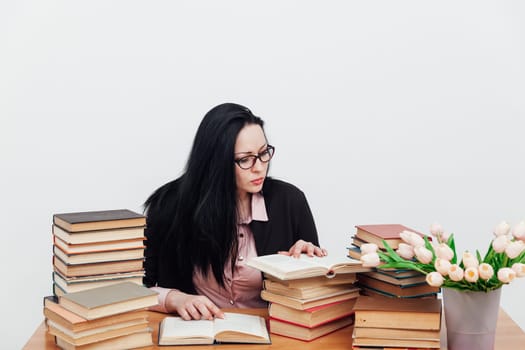 a teacher with glasses sits at a table near a stack of books and reads a book scientific work preparation for exams