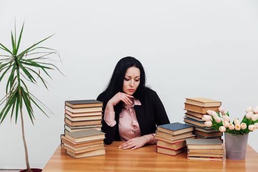 a woman sitting at a table with a stack of books many books cabinet library