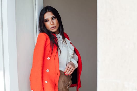 a woman fashionable brunette in a bright jacket business style in the office stands against the wall