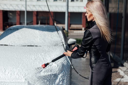 blonde woman washes a car at a car wash clean car water in a hose for a car