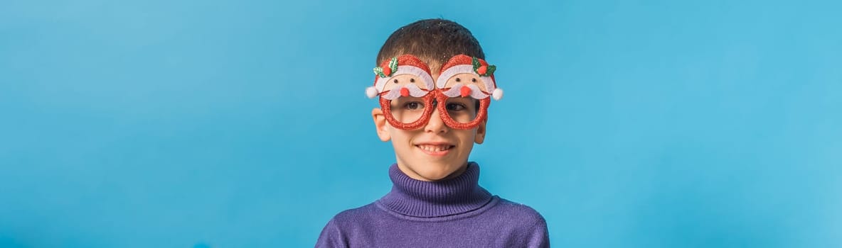 Cute little child boy in party Christmas Santa Claus glasses on blue background. Kid with snow on head copy space and mockup.