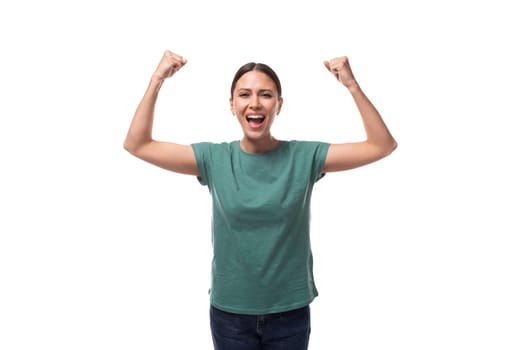well-groomed slender young brunette woman dressed in a green T-shirt is emotionally aroused and raised her hands.