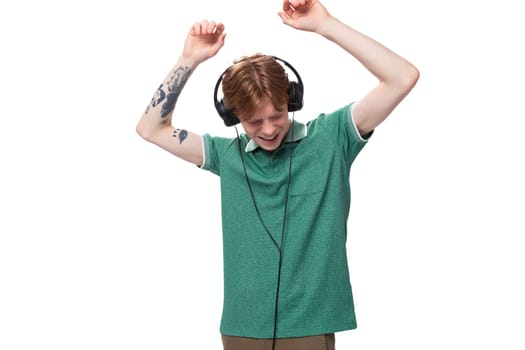 a young man with red hair dressed in a green t-shirt in wireless large headphones dances and enjoys.