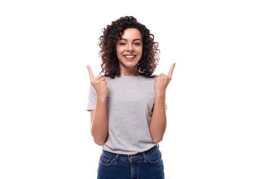young european woman with black curly hair in a gray basic t-shirt looks happy on a white background.