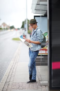Man, journey and bus stop with map, travel and adventure by commute, transportation and planning for trip. Male person, information and guide for direction, navigation and vacation or earphones.