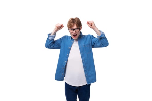 portrait of a joyful european red-haired student guy dressed in a blue denim shirt on a white studio background.