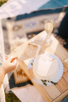 Piece of wedding cake on a wooden board in the bride hand. Cropped. Faceless. High quality photo