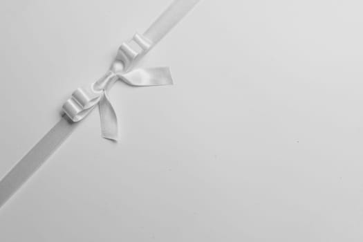Elegant satin white ribbon bow on gray background