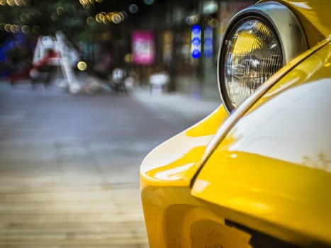 close up on old vintage yellow car ,front light over public area space with bokeh light