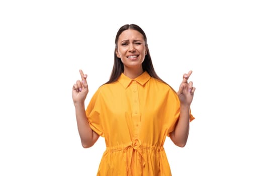 pretty young brunette lady wearing a bright yellow short sleeve dress crossed her fingers in anticipation.