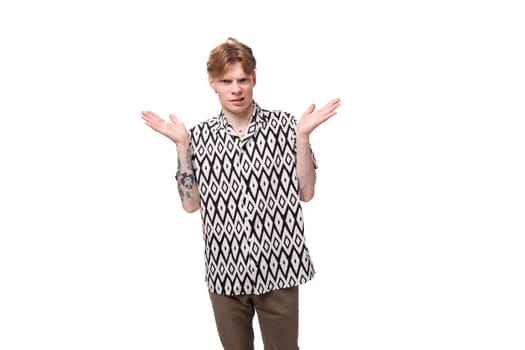 portrait of a pensive smart young informal guy with red hair and a tattoo on his arms is dressed in a short-sleeved shirt with a pattern.