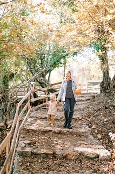 Smiling mother walks holding hands with a little girl along the steps of the park with a bowl in her hand. High quality photo