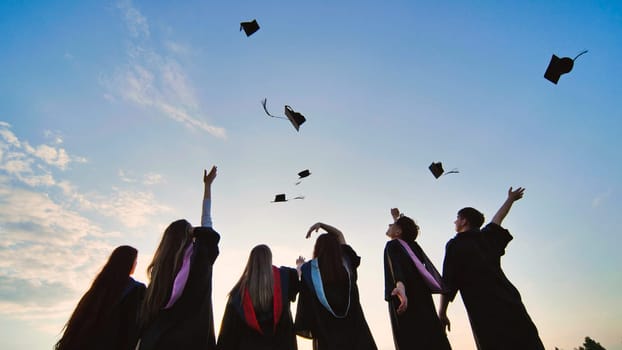 Student graduates toss their caps at sunset