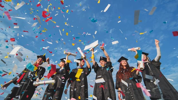 Graduates throw colorful confetti against a blue sky