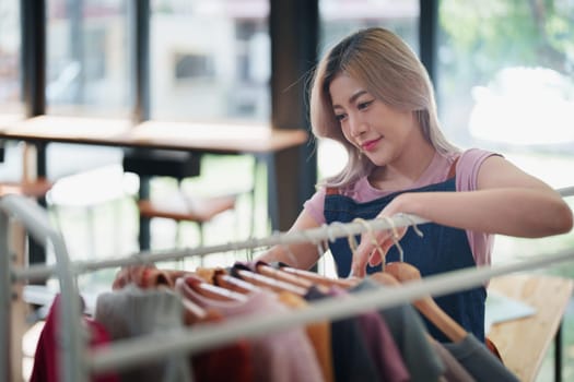 Portrait Of Asian Female Owner Of Fashion Store Checking Stock In Clothing Store With using notebook successful happy smile at small business, sme or ecommerce concepts.