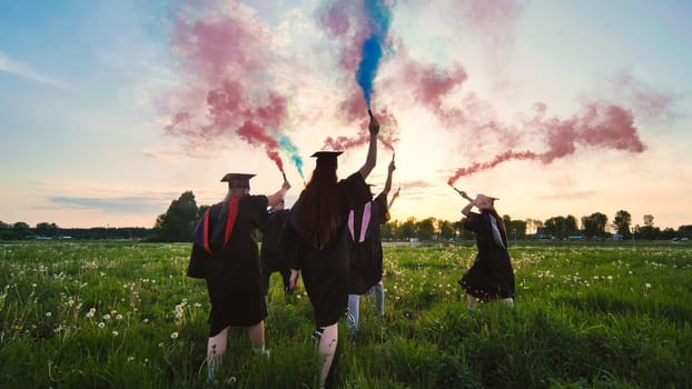 Graduates in costume walk with a smoky multi-colored smoke at sunset.