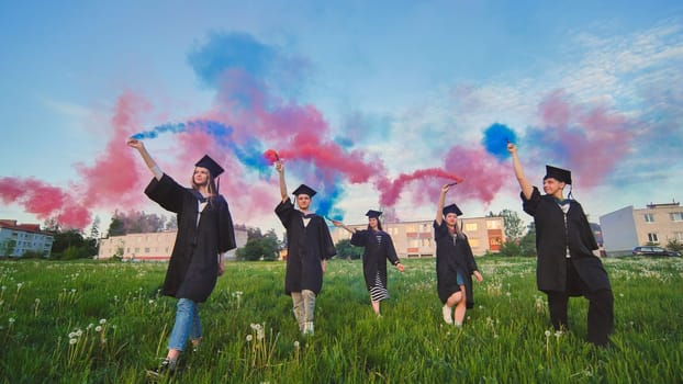 Graduates in costume walk with a smoky multi-colored smoke at sunset.