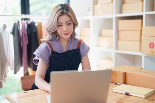 Starting small business entrepreneur of independent young Asian woman online seller is using computer and taking orders to pack products for delivery to customers. SME delivery concept.