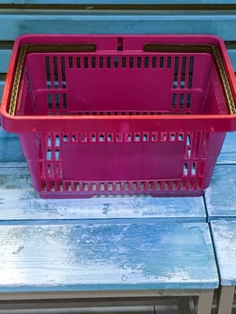 An empty red plastic shopping basket stands on the packing table, close-up, space for text from below.