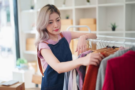 Portrait Of Asian Female Owner Of Fashion Store Checking Stock In Clothing Store With using notebook successful happy smile at small business, sme or ecommerce concepts.