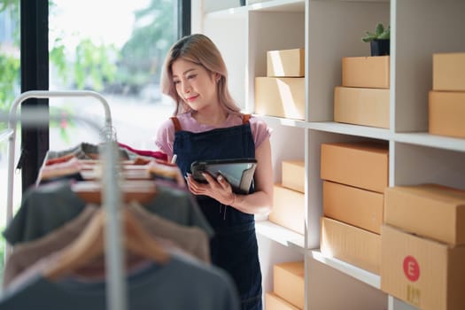 Portrait Of Asian Female Owner Of Fashion Store Checking Stock In Clothing Store With using notebook successful happy smile at small business, sme or ecommerce concepts.