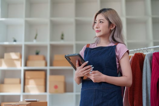 Portrait Of Asian Female Owner Of Fashion Store Checking Stock In Clothing Store With using notebook successful happy smile at small business, sme or ecommerce concepts.