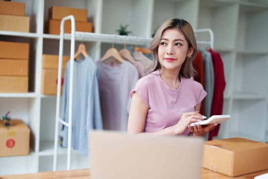 Portrait Of Asian Female Owner Of Fashion Store Checking Stock In Clothing Store With using notebook successful happy smile at small business, sme or ecommerce concepts.