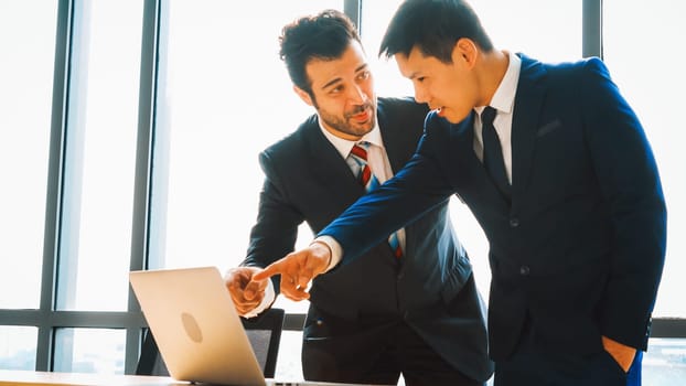 Two business people talk project strategy at office meeting room. Businessman discuss project planning with colleague at modern workplace while having conversation and advice on financial report. Jivy