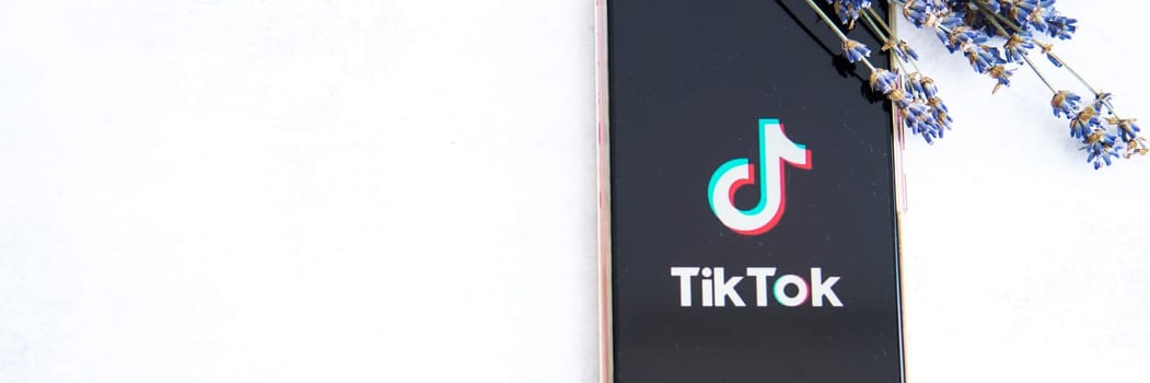 Tver, Russia-August 5, 2020, the tik tok logo on the smartphone screen on light background with lavender flowers. Tick-Tok icon. logo of the current app. Tiktok social network.