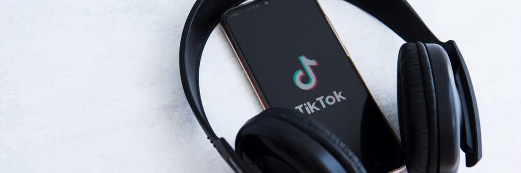 Tver, Russia-August 5, 2020, the tik tok logo on the smartphone screen on light background with large headphones. Tik-Tok icon. logo of the current app. Tiktok social network.