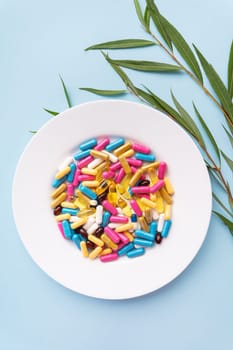 Many colorful pills, nutritional supplements in a white plate on a blue background. Prescription medicine, vertical photo