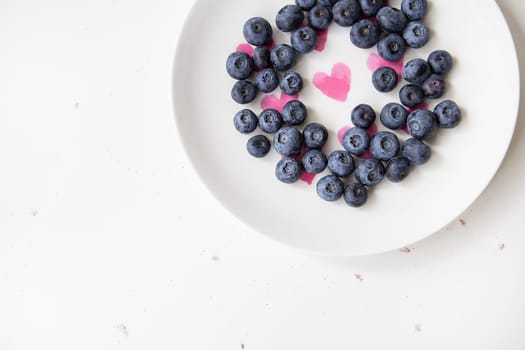 Delicious blueberries lie on a plate with a heart inside. Delicious and healthy food. Place for an inscription