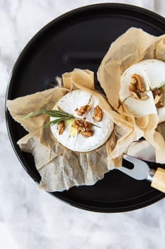 Baked camembert with walnuts and honey wrapped in parchment lies on a grill stand, delicious and healthy food