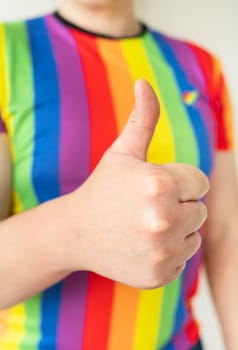 A young guy in a lgbt flag color t-shirt raises a clenched fist and shows like. Lgbt concept, people lifestyle