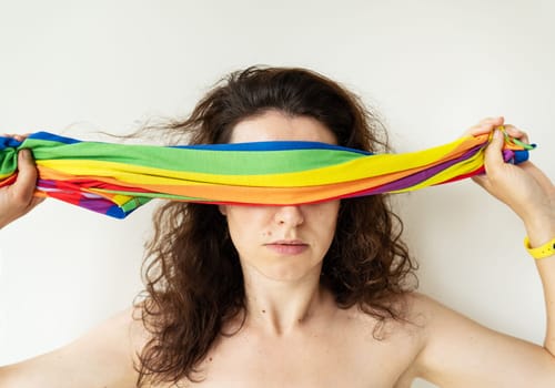 A girl covers her eyes with a bright multi-colored rainbow LGBT flag. LGBT girl. There is no support from society for hiding your sexuality