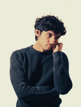 A man with curly hair wearing a black sweater, thinking, or disappointed or sad, in studio shot