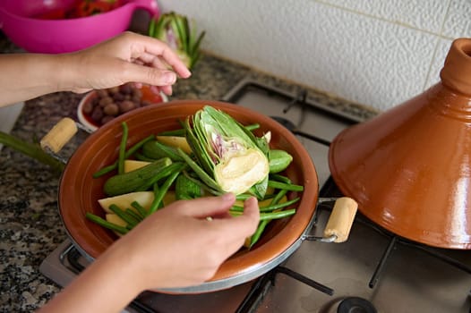 Close-up hands of unrecognizable woman housewife, chef cooking traditional Moroccan meal in tagine clay dish, standing by marble kitchen counter. Food background. Veganism and vegetarianism