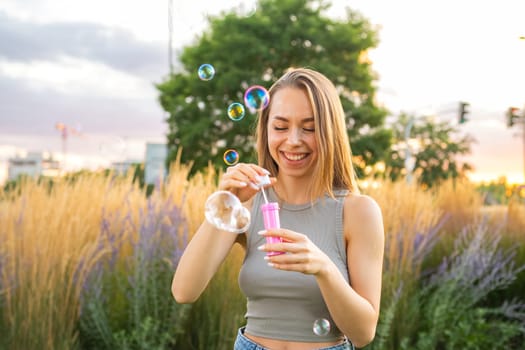 A happy young woman with flowing hair blows soap bubbles and laughing