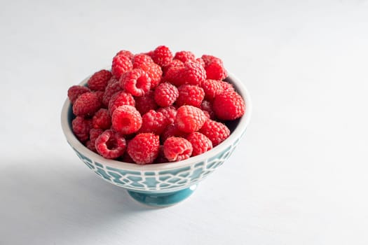 fresh raspberries in a blue bowl at the white table, summer harvest fruits and fresh berries, vitamins, vegetarian concept, High quality photo