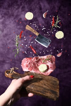 Art photo levitation of a meat steak with ingredients for frying oil spices rosemary pepper garlic on a lilac background. High quality photo